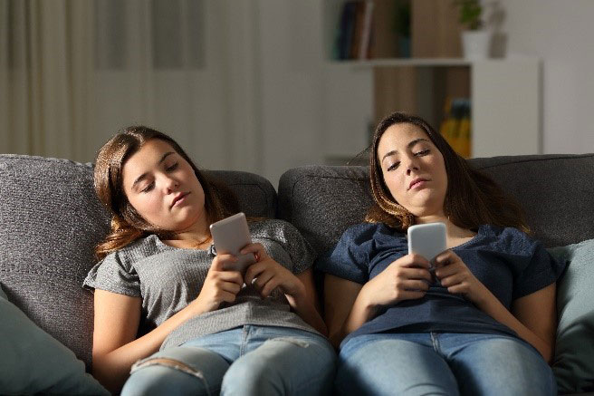 two women on a couch looking at their cell phones.