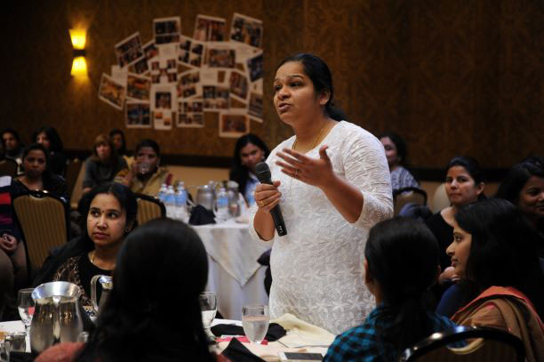 a woman standing up at a table and giving a speech.