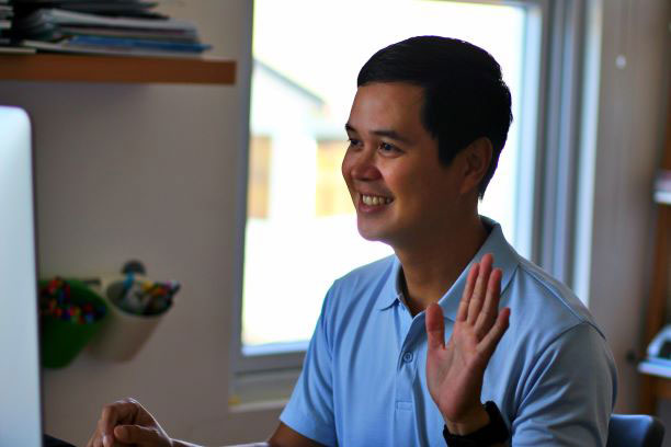 man waving hello to his computer screen during a virtual event.